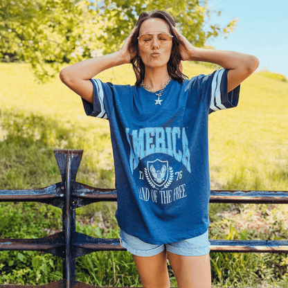 Land of the Free jersey tee in navy blue with white stripes, featuring a graphic print and model posing outdoors.
