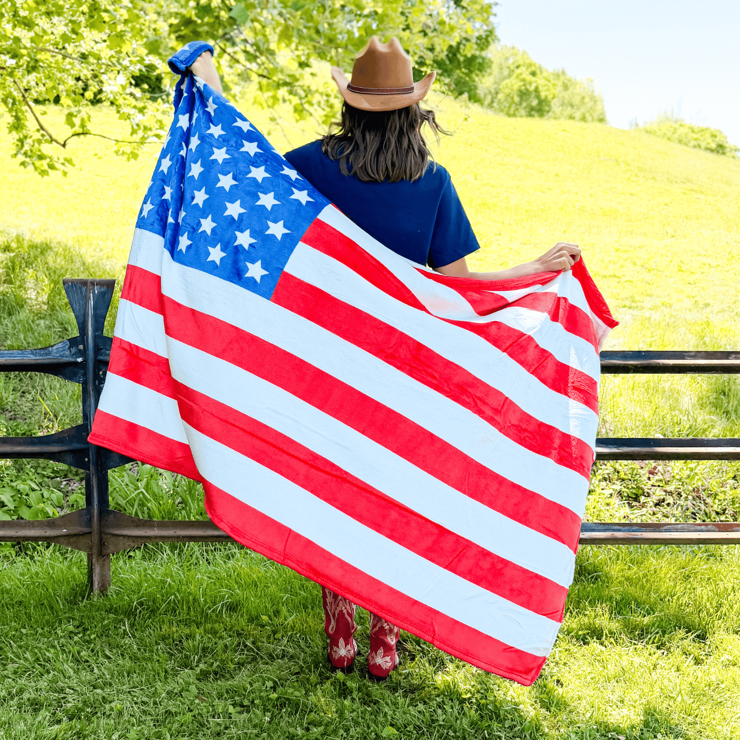 Cozy Flag fleece blanket displayed by a person wearing a cowboy hat, featuring a red and white striped design with blue st...